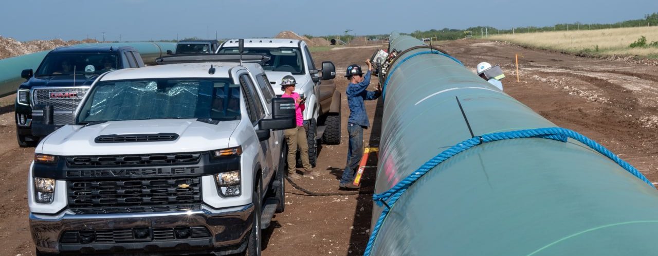Prime crew mounting an automated ultrasonic scanner on a coated pipe string on a pipeline right-of-way