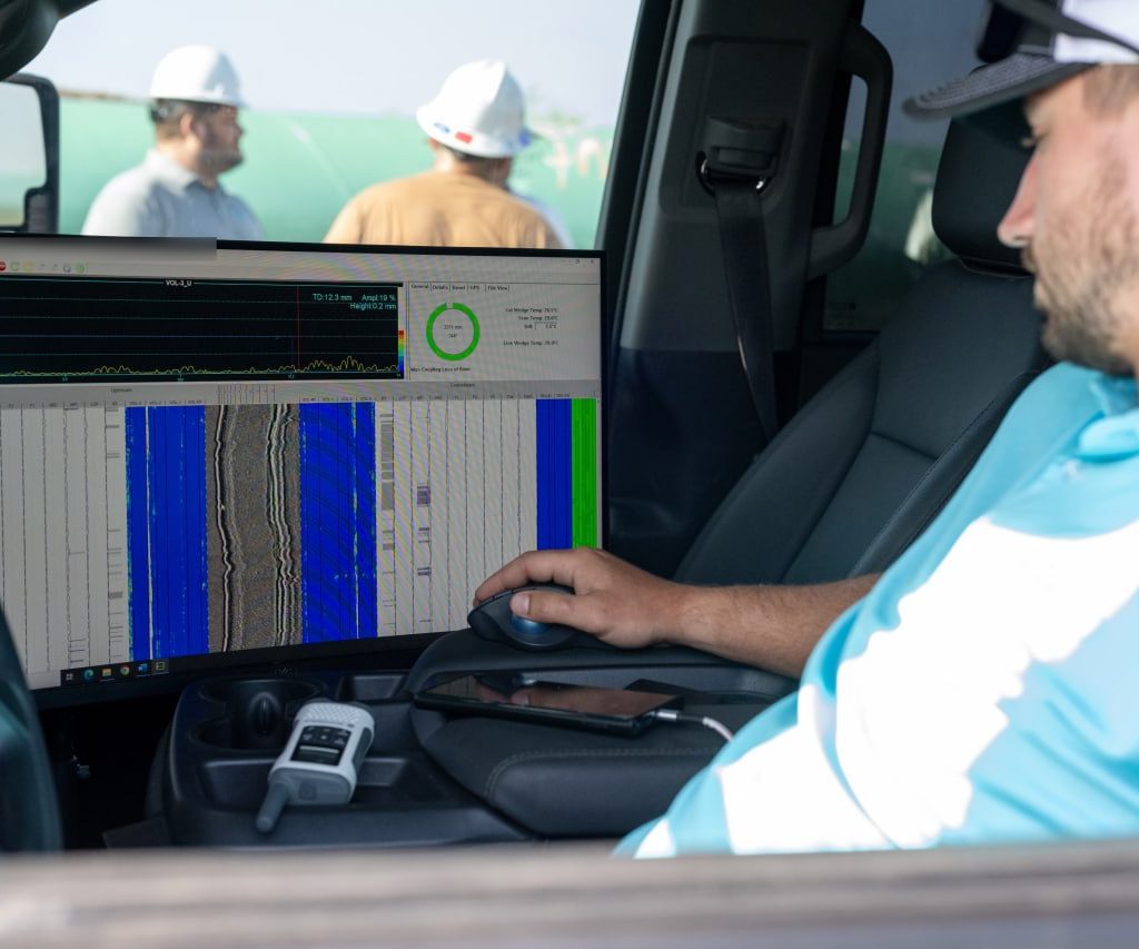 Prime Inspections technician reviewing an encoded ultrasonic scan on screen in the inspection truck, with crew working outside