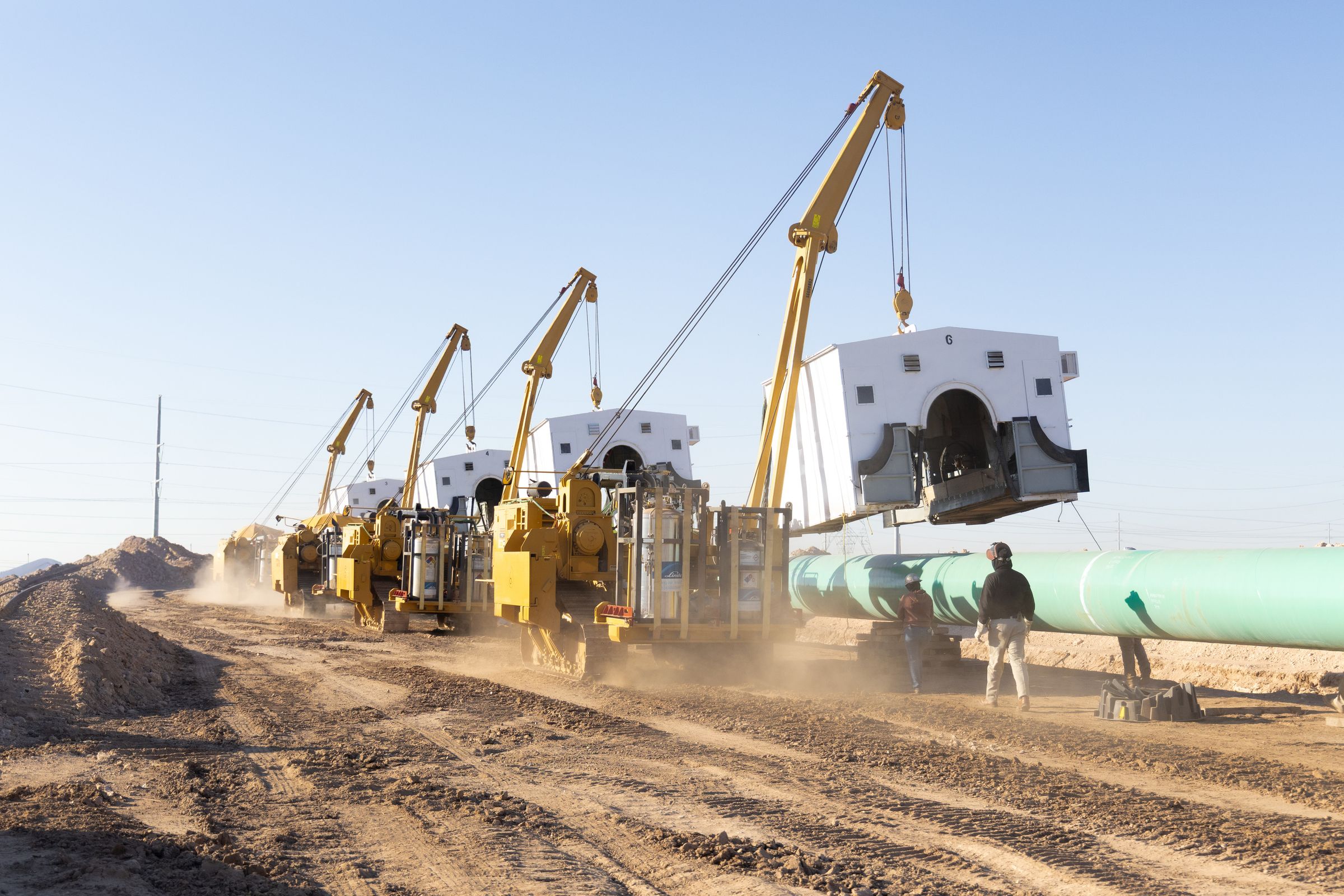 Sidebooms carrying weld shacks along a pipeline right-of-way
