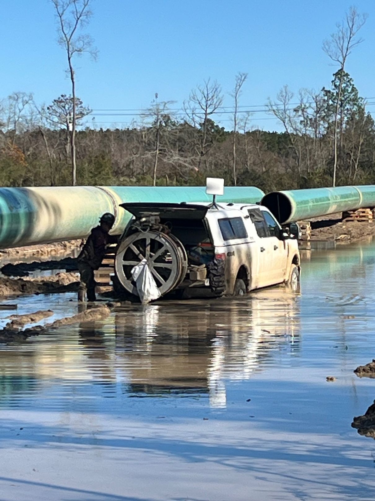 Prime Inspections truck working through standing water beside a large-diameter pipeline
