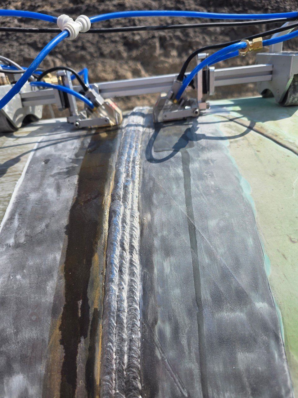 Phased-array scanner on a girth weld, riding the weld cap with couplant lines attached