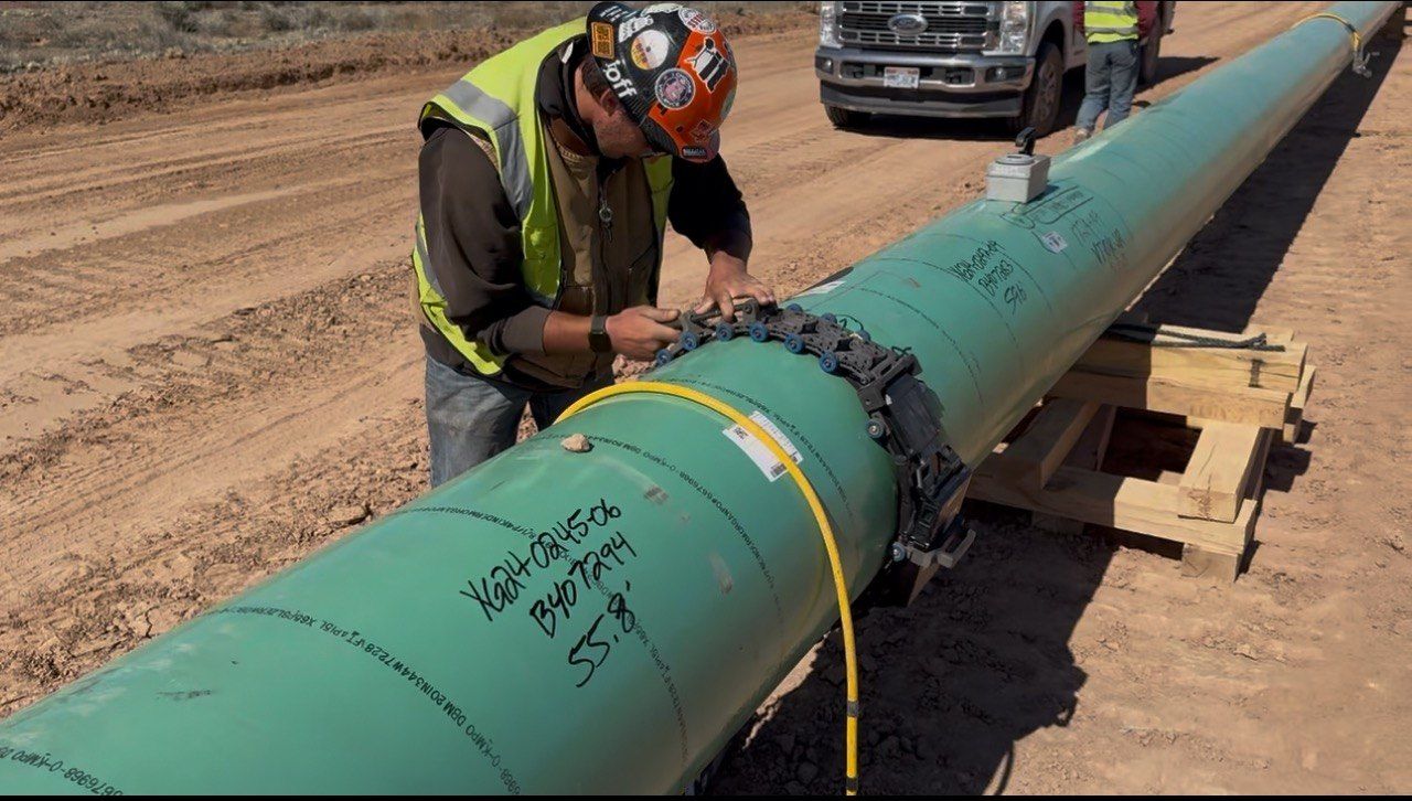 Technician mounting an inspection band on a pipeline girth weld, with a Prime Inspections truck behind