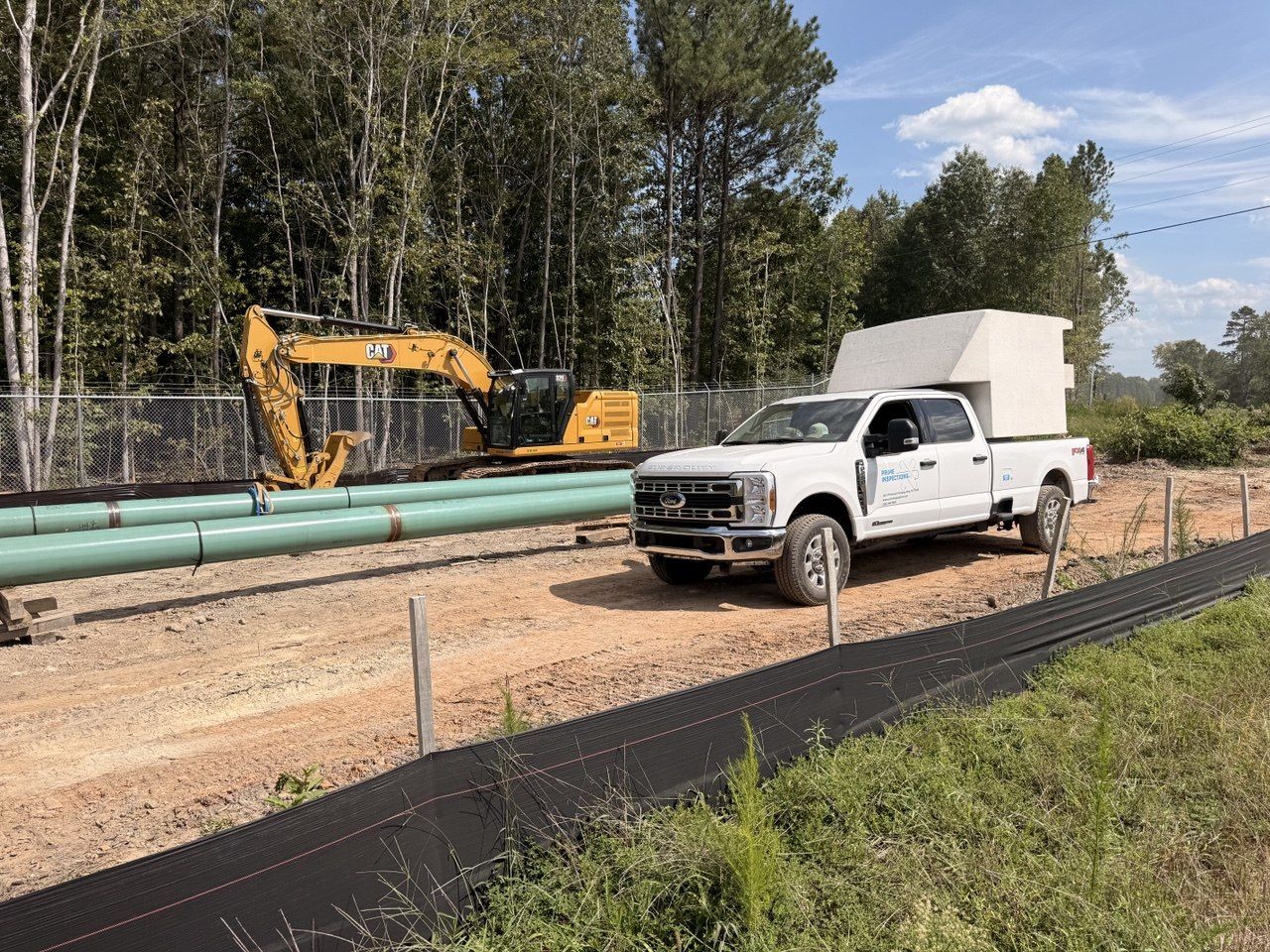 Prime Inspections darkroom truck on a pipeline right-of-way beside the pipe string, with an excavator working alongside