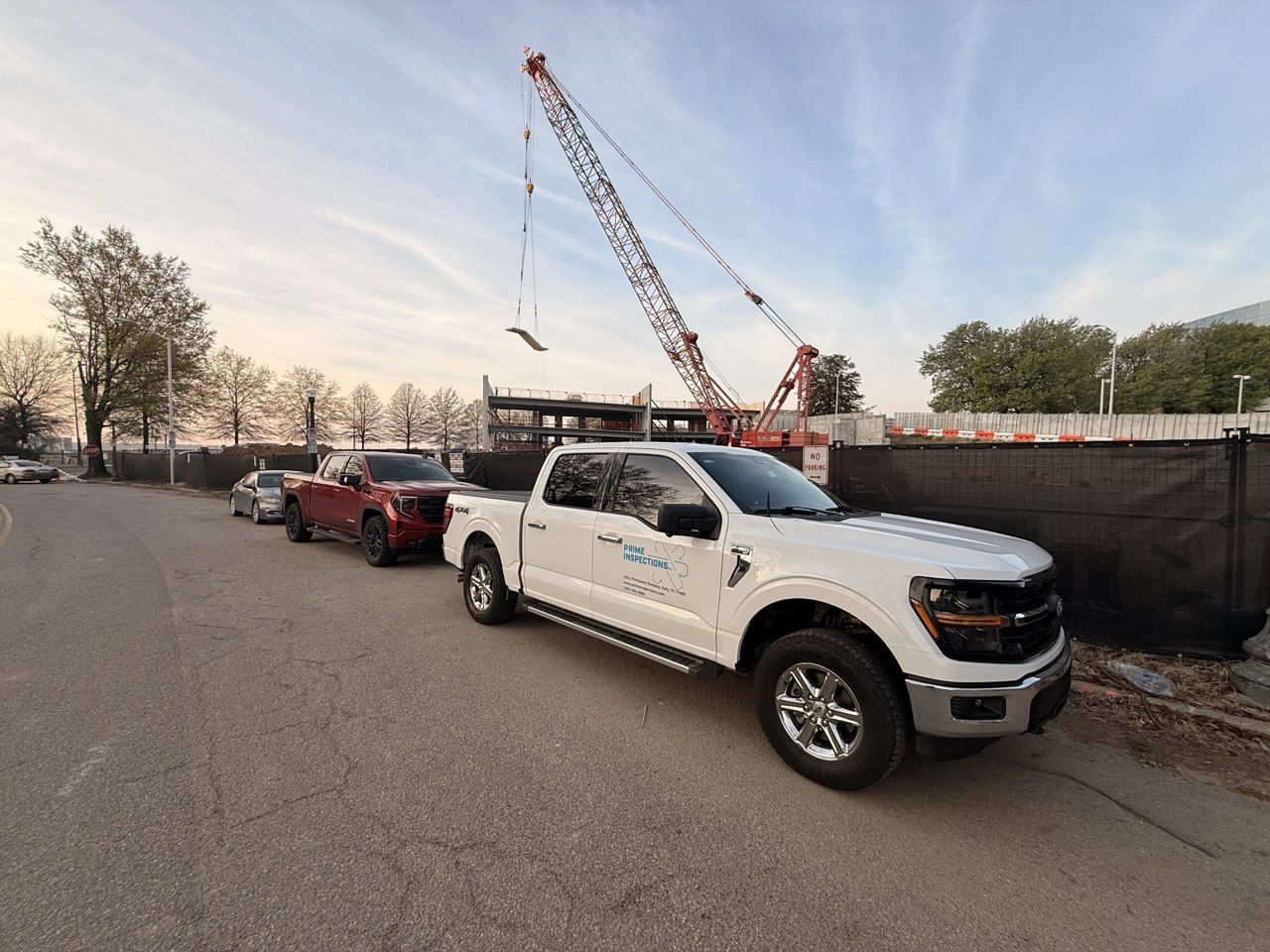 Prime Inspections truck parked at an industrial construction site with a crawler crane at dusk